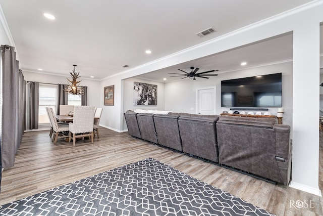 living room featuring ceiling fan with notable chandelier, wood-type flooring, and ornamental molding