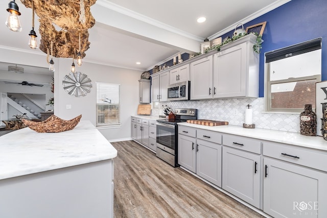 kitchen with hanging light fixtures, light wood-type flooring, ornamental molding, gray cabinets, and stainless steel appliances