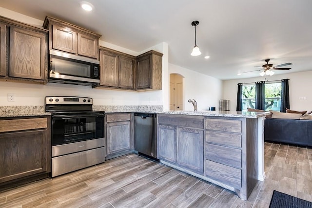 kitchen with appliances with stainless steel finishes, dark brown cabinetry, light stone countertops, decorative light fixtures, and kitchen peninsula