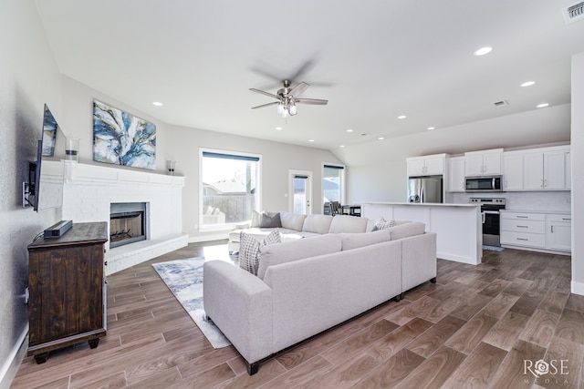 living room featuring a brick fireplace, vaulted ceiling, and ceiling fan