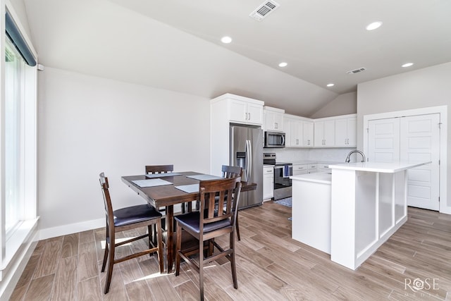 kitchen with stainless steel appliances, an island with sink, vaulted ceiling, and white cabinets