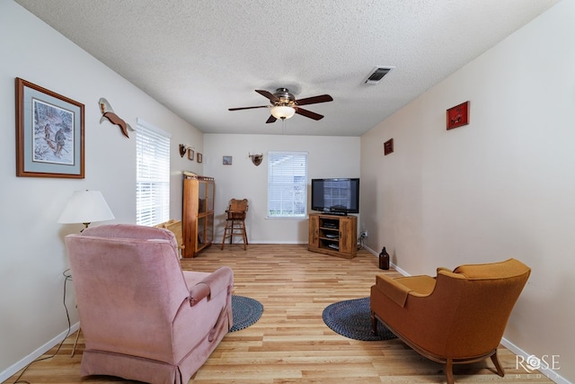 living room with ceiling fan, light hardwood / wood-style floors, and a textured ceiling