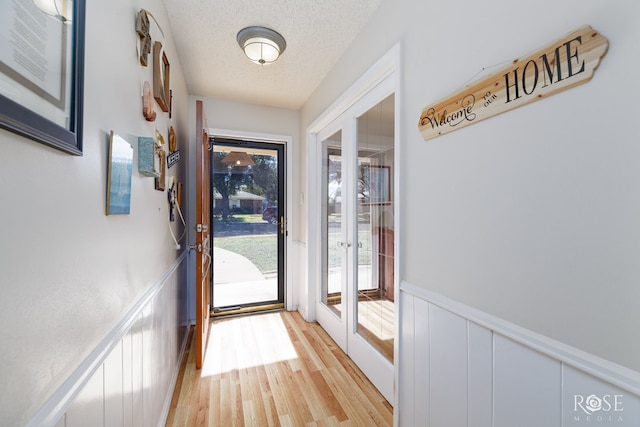 doorway to outside with a wealth of natural light, light hardwood / wood-style floors, and a textured ceiling