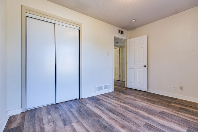 unfurnished bedroom with dark wood-type flooring, a textured ceiling, and a closet