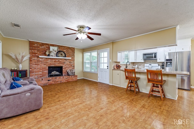 2713 Canyon Creek Dr, San Angelo, TX 76904 - living room with light wood-type flooring, crown molding, ceiling fan, a textured ceiling, and a fireplace