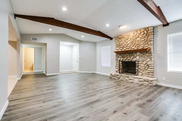 unfurnished living room featuring a stone fireplace, lofted ceiling with beams, a textured ceiling, and light wood-type flooring