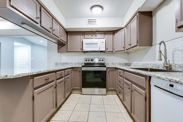 kitchen featuring sink, white appliances, light stone counters, a textured ceiling, and kitchen peninsula