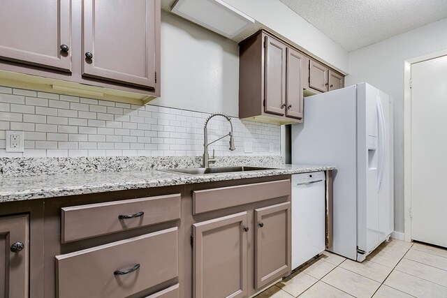 kitchen featuring sink, decorative backsplash, light tile patterned floors, white appliances, and a textured ceiling