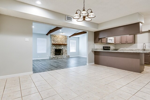 kitchen with a stone fireplace, tasteful backsplash, light tile patterned floors, kitchen peninsula, and beam ceiling