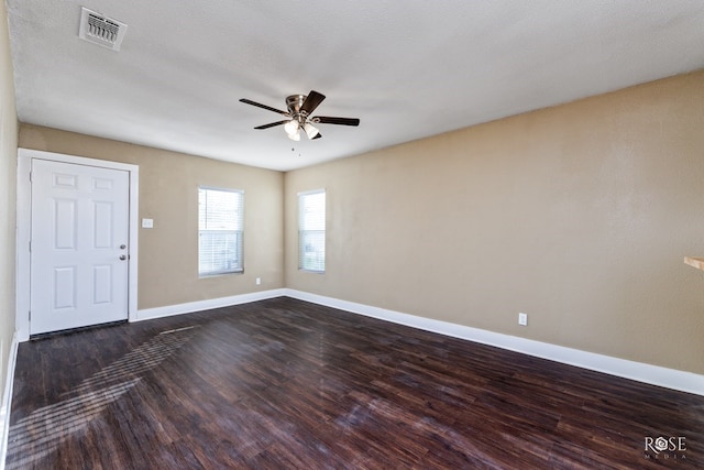 empty room with baseboards, visible vents, dark wood finished floors, a ceiling fan, and a textured ceiling