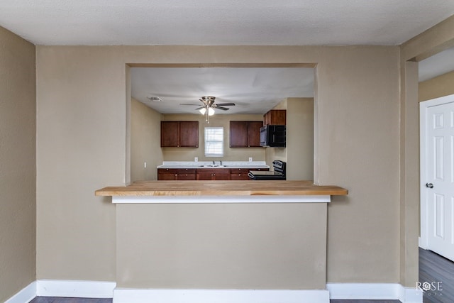 kitchen featuring baseboards, a peninsula, light countertops, a sink, and range with electric stovetop