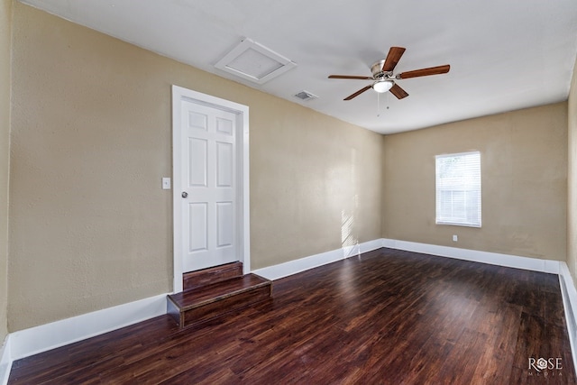 unfurnished room with dark wood-style floors, visible vents, attic access, ceiling fan, and baseboards