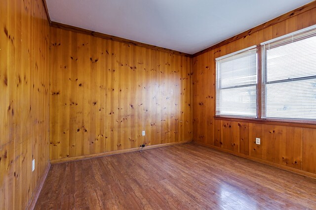 empty room with hardwood / wood-style flooring, crown molding, and wooden walls