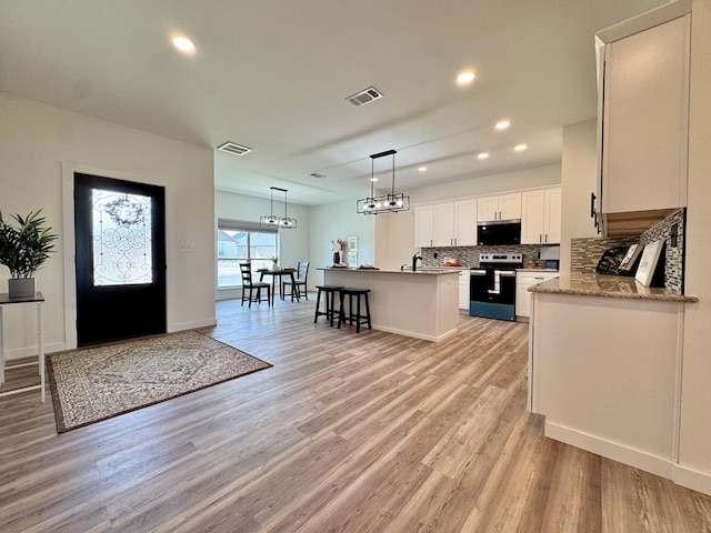 3634 Silver Spur Dr, San Angelo, TX 76904 - kitchen with appliances with stainless steel finishes, tasteful backsplash, light wood finished floors, an island with sink, and white cabinetry