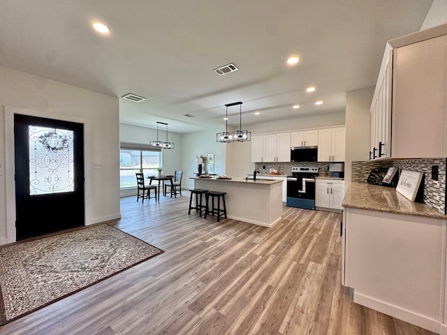 3634 Silver Spur Dr, San Angelo, TX 76904 - kitchen featuring stainless steel appliances, tasteful backsplash, a kitchen island with sink, light wood finished floors, and white cabinetry