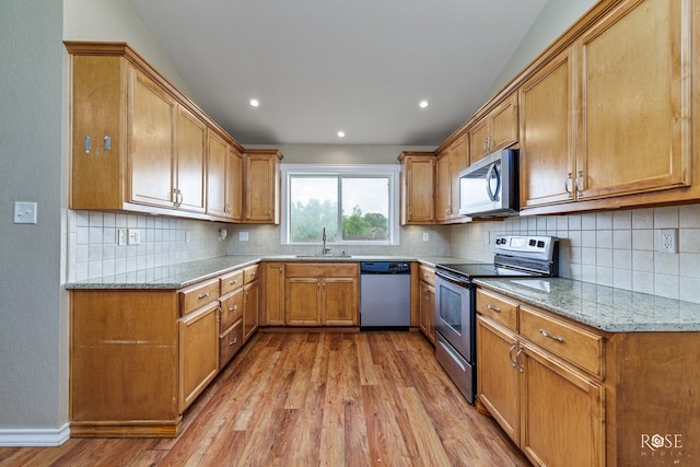 4506 Oak Grove Blvd, San Angelo, TX 76904 - kitchen with backsplash, appliances with stainless steel finishes, a sink, light stone counters, and light wood-style floors