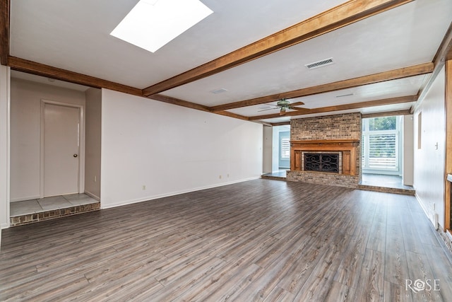 unfurnished living room featuring hardwood / wood-style flooring, ceiling fan, a skylight, a brick fireplace, and beamed ceiling