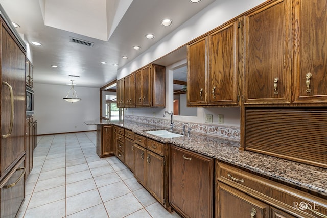 kitchen with sink, light tile patterned floors, decorative light fixtures, kitchen peninsula, and dark stone counters