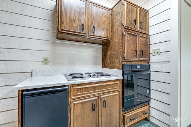 kitchen with black oven, white cooktop, and wooden walls