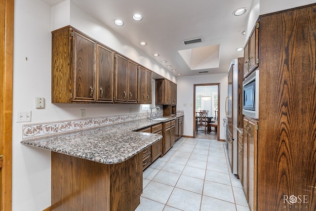 kitchen with stainless steel microwave, sink, dark stone countertops, light tile patterned floors, and kitchen peninsula