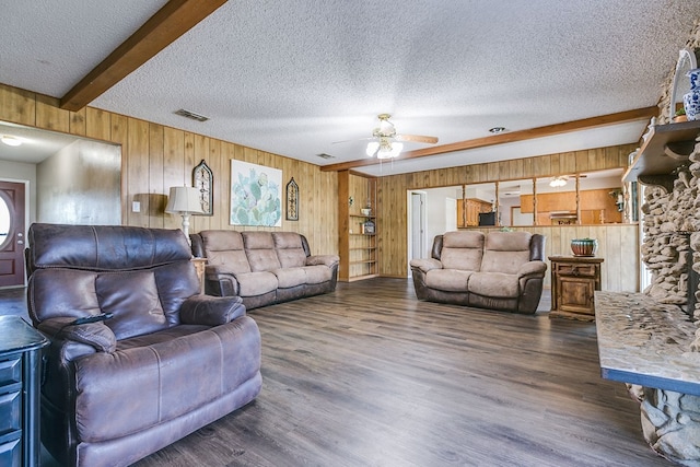 living room featuring dark wood-type flooring, wood walls, a textured ceiling, ceiling fan, and beam ceiling