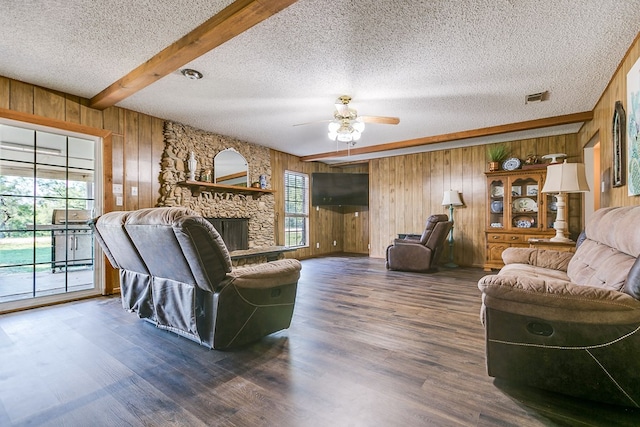 living room with beamed ceiling, a stone fireplace, dark wood-type flooring, and wood walls