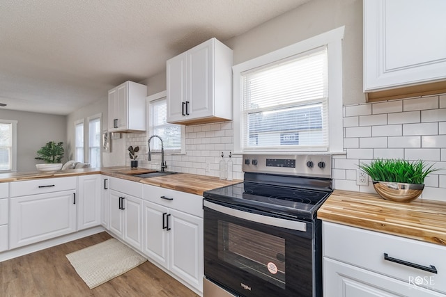 kitchen with a sink, light wood-type flooring, a textured ceiling, butcher block counters, and stainless steel electric range
