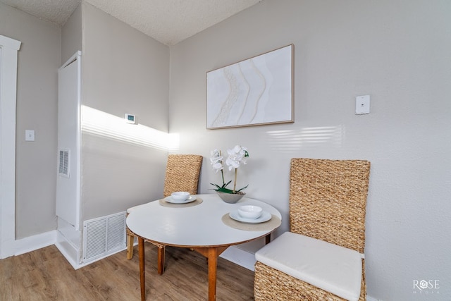 dining area with a textured ceiling, wood finished floors, baseboards, and visible vents