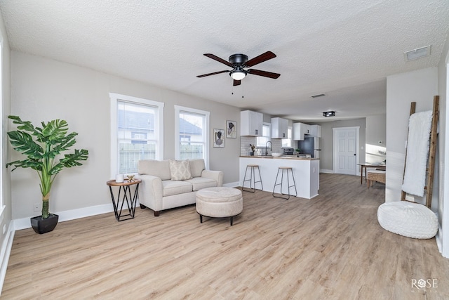 living room featuring light wood-style floors, a ceiling fan, visible vents, and a textured ceiling
