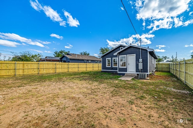 back of house featuring a yard, a fenced backyard, central AC, and an outbuilding