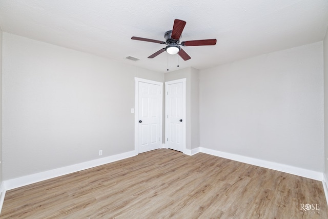 empty room with wood finished floors, ceiling fan, baseboards, and visible vents