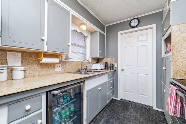 kitchen featuring wine cooler, crown molding, gray cabinetry, a sink, and a textured ceiling