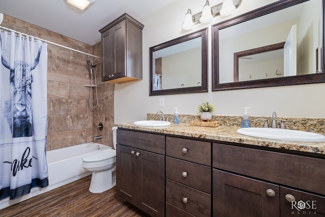 full bath with toilet, double vanity, a sink, and wood finished floors