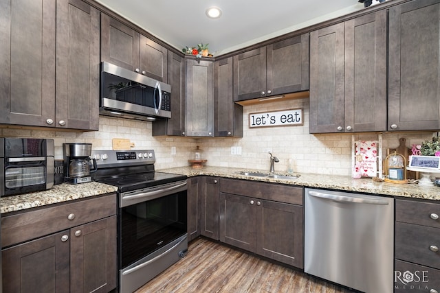 kitchen with wood finished floors, a sink, stainless steel appliances, dark brown cabinets, and backsplash