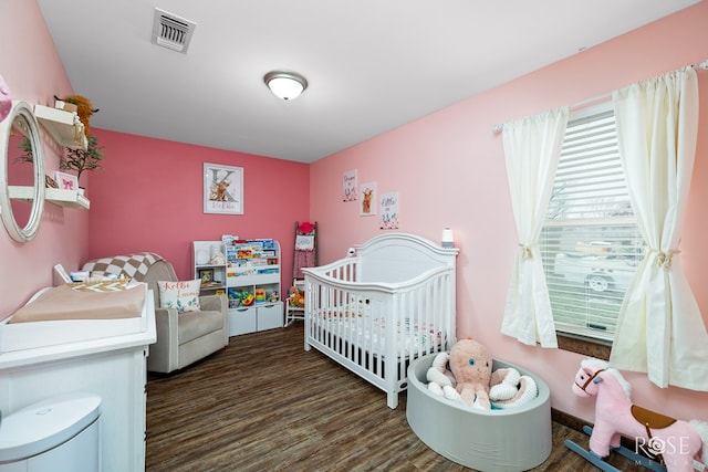 bedroom with a nursery area, wood finished floors, and visible vents