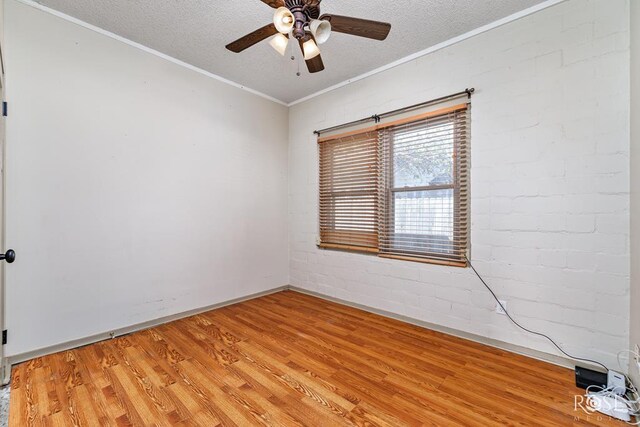 spare room with crown molding, wood-type flooring, a textured ceiling, and brick wall