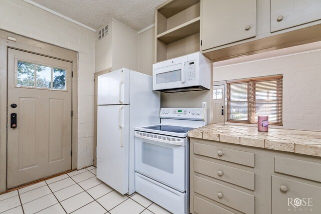 kitchen with brick wall, tile counters, light tile patterned floors, white appliances, and a textured ceiling