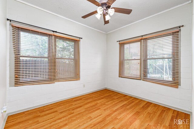 empty room with wood-type flooring, a textured ceiling, ornamental molding, ceiling fan, and brick wall