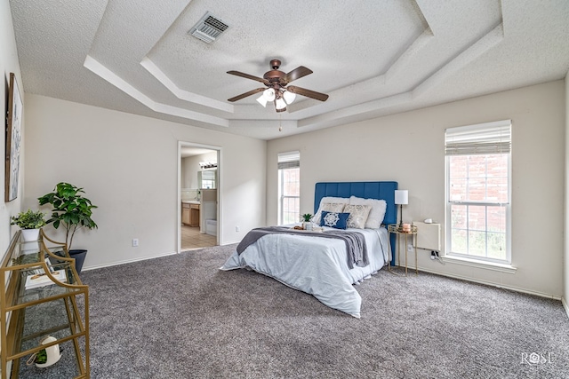 5221 Coral Way, San Angelo, TX 76904 - carpeted bedroom featuring a tray ceiling, a textured ceiling, baseboards, ensuite bath, and a ceiling fan
