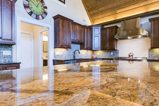 kitchen featuring lofted ceiling, sink, dark stone countertops, dark brown cabinets, and wall chimney range hood