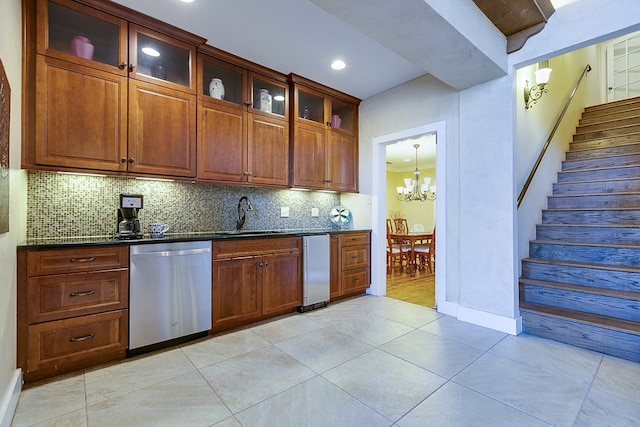 kitchen with sink, light tile patterned floors, dark stone countertops, dishwasher, and a notable chandelier