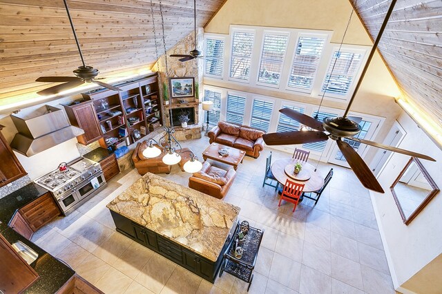 living room featuring ceiling fan, a towering ceiling, a fireplace, and light tile patterned floors