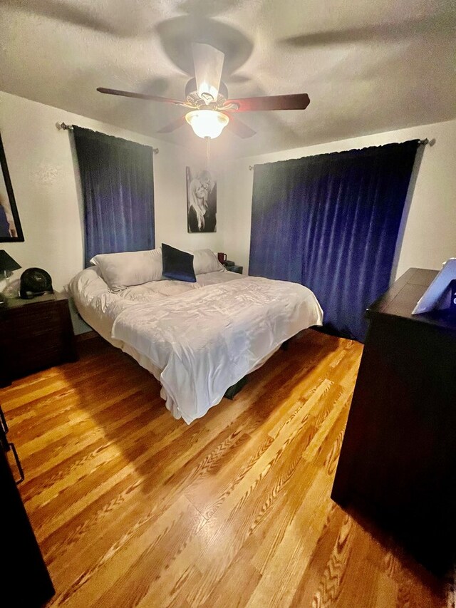 bedroom with ceiling fan, wood-type flooring, and a textured ceiling