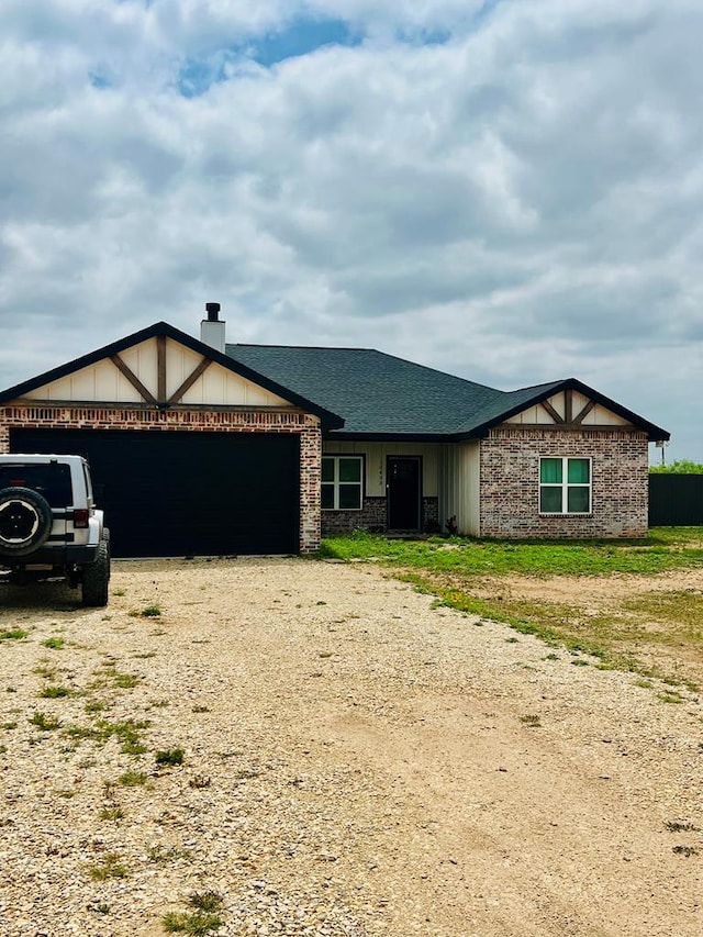 view of front of house with a garage, dirt driveway, and roof with shingles