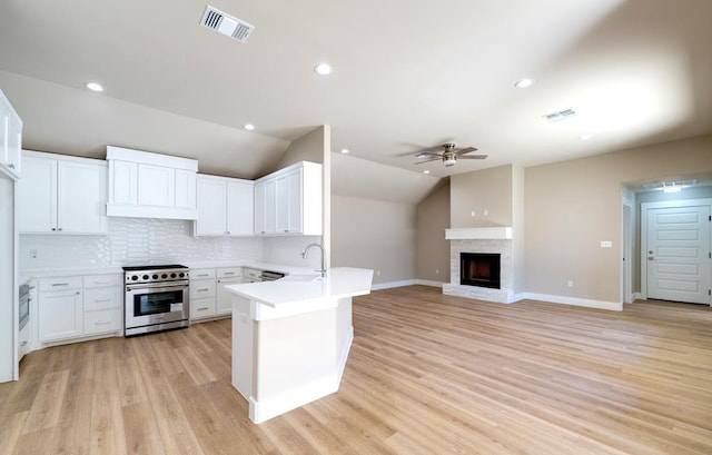 kitchen with vaulted ceiling, stainless steel stove, white cabinetry, sink, and kitchen peninsula