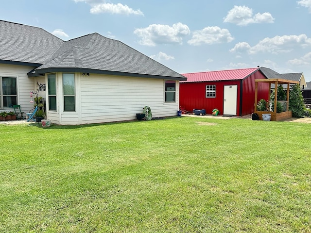 rear view of house featuring roof with shingles, a lawn, and an outdoor structure