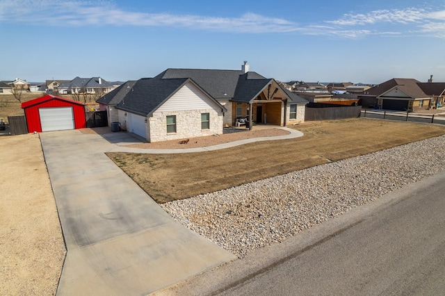 view of front of house with stone siding, concrete driveway, fence, and a residential view