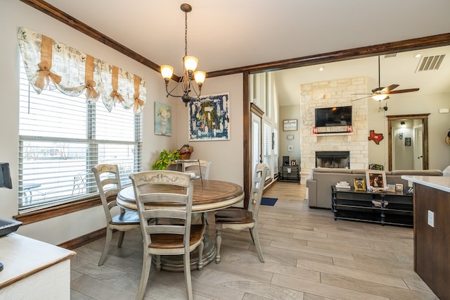 dining room with light wood finished floors, visible vents, ornamental molding, a stone fireplace, and baseboards