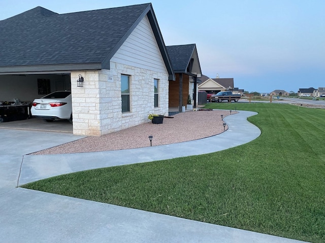 view of side of home featuring a garage, concrete driveway, stone siding, roof with shingles, and a lawn