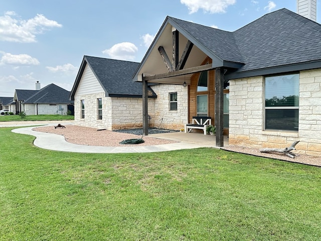 back of house featuring a shingled roof, stone siding, a patio area, and a lawn